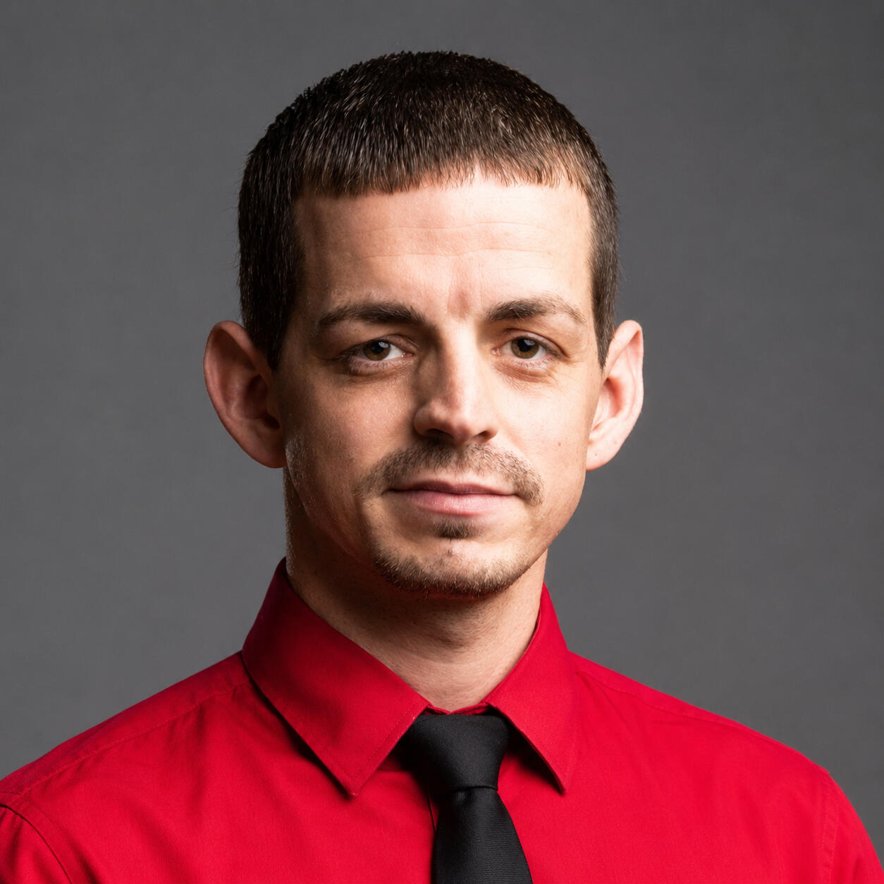 Josh Centanni – Author and Speaker Headshot Professional headshot of Josh Centanni, an author and speaker, wearing a red dress shirt with a black necktie against a solid dark gray studio background.