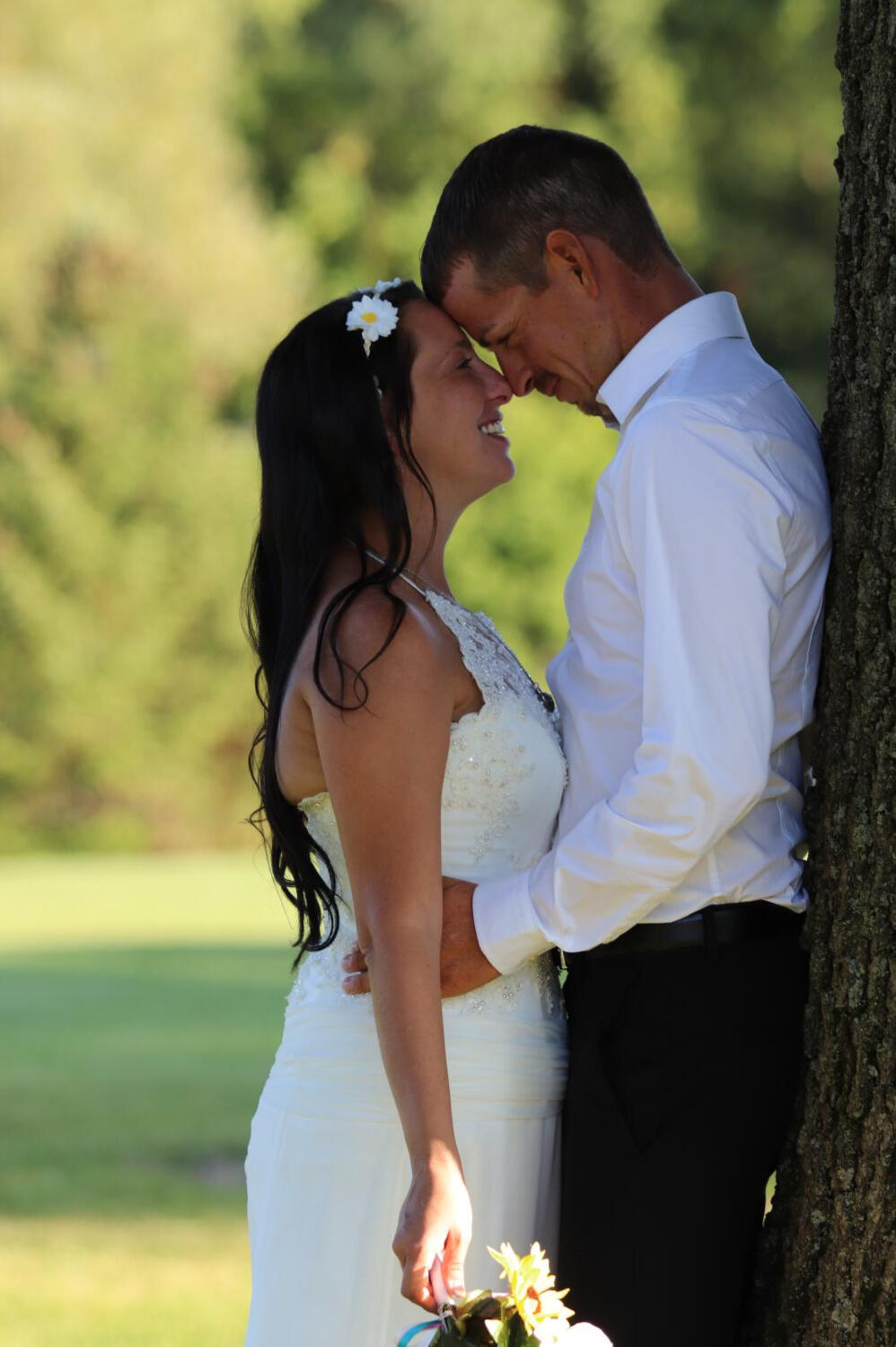 Kadi Centanni and Josh Centanni Wedding Day – August 2019 Close-up portrait of a bride and groom smiling warmly at each other with their foreheads together under a tree, with a soft blurred green grass background.